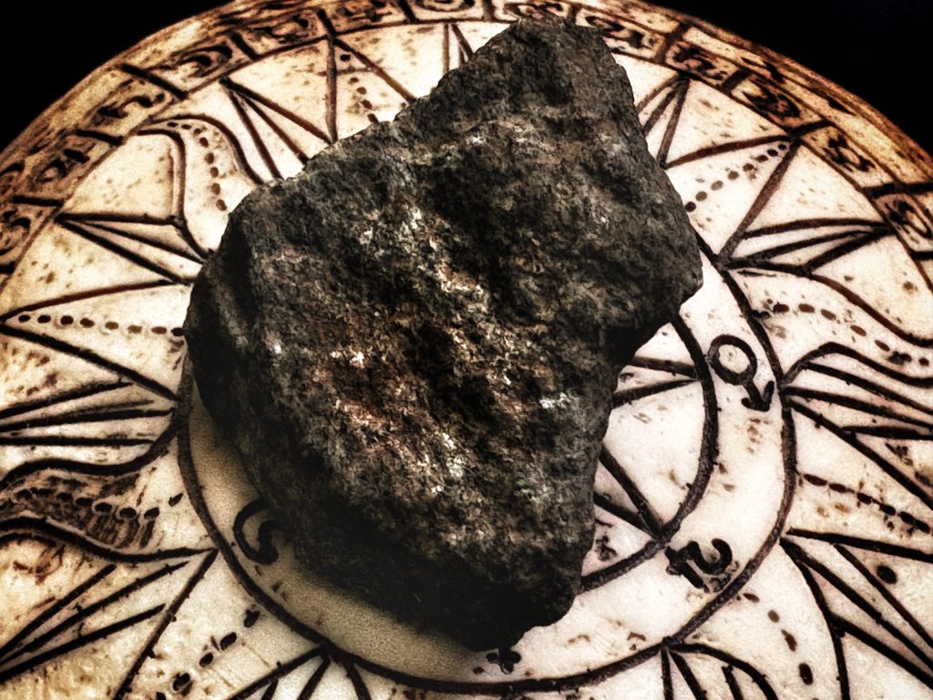 A dark stone rests on an elaborate carved design with astrological symbols amidst a partially obscured image of a sun's rays and a five-pointed star.